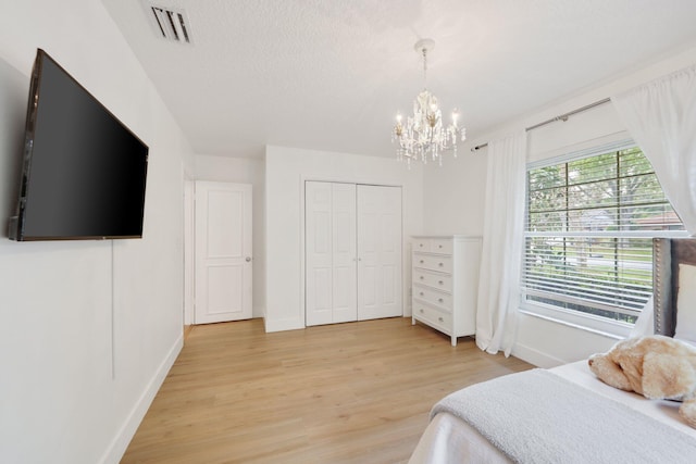 bedroom with a textured ceiling, visible vents, baseboards, a closet, and light wood finished floors