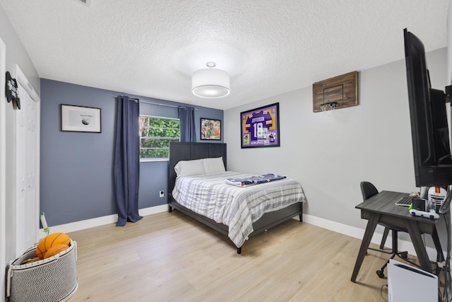 bedroom with light wood-style floors, baseboards, and a textured ceiling