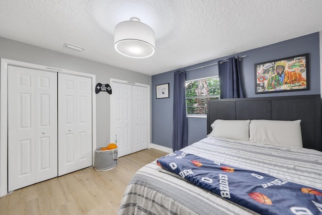 bedroom featuring wood finished floors, a textured ceiling, baseboards, and two closets