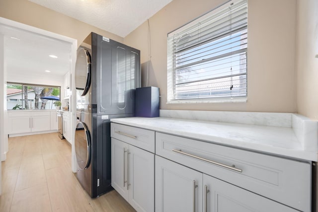 laundry area featuring light wood-type flooring, cabinet space, a textured ceiling, and stacked washer / drying machine