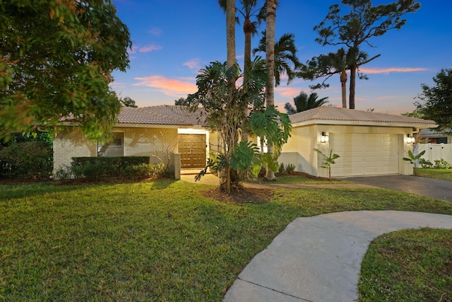 view of front of property featuring an attached garage, brick siding, driveway, a yard, and a tiled roof