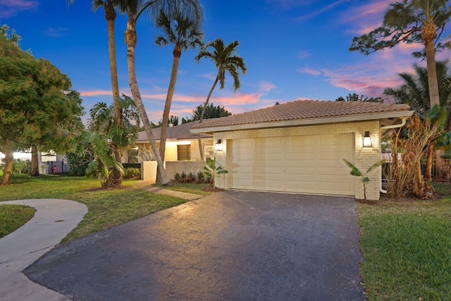 view of front of property with an attached garage, aphalt driveway, a lawn, and brick siding