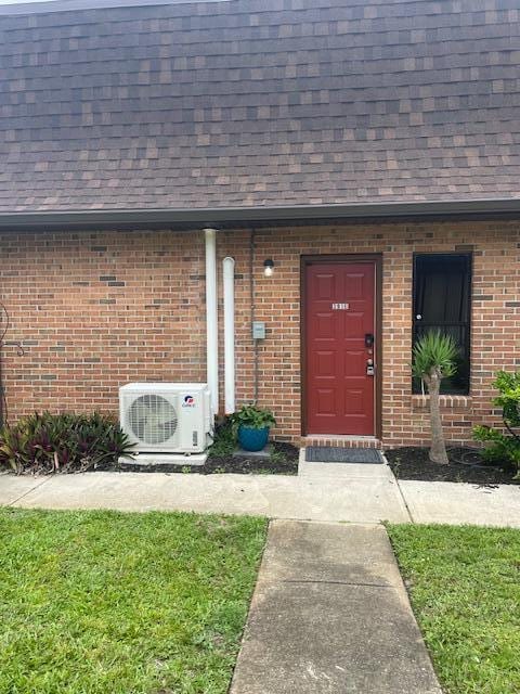 property entrance with ac unit, roof with shingles, and brick siding