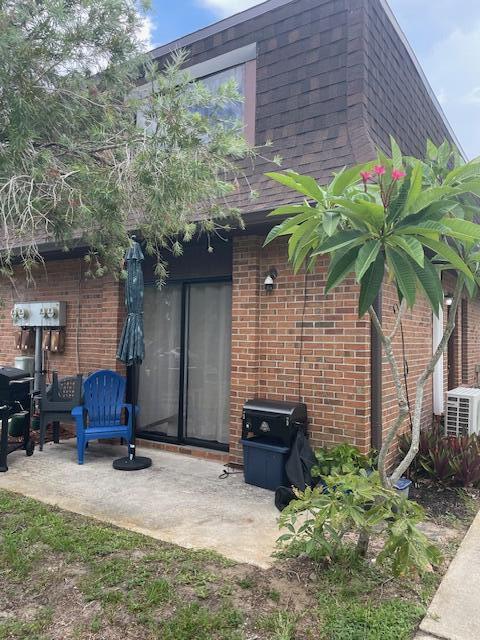 exterior space featuring roof with shingles, mansard roof, a patio, and brick siding