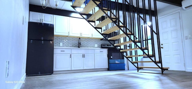 kitchen featuring a wall unit AC, light wood-style floors, white cabinets, and freestanding refrigerator