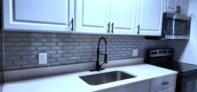 kitchen with stainless steel appliances, light countertops, backsplash, white cabinetry, and a sink