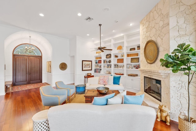 living area featuring visible vents, built in features, wood-type flooring, a premium fireplace, and ceiling fan with notable chandelier