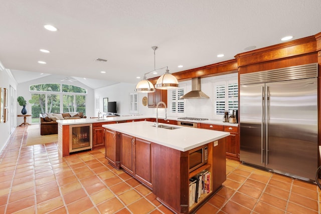 kitchen with beverage cooler, appliances with stainless steel finishes, open floor plan, wall chimney range hood, and a sink