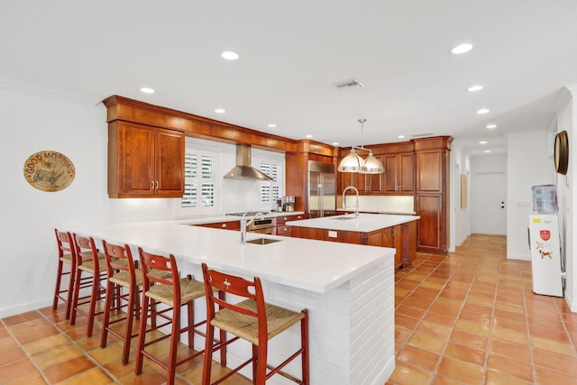 kitchen with built in fridge, visible vents, wall chimney range hood, decorative backsplash, and an island with sink