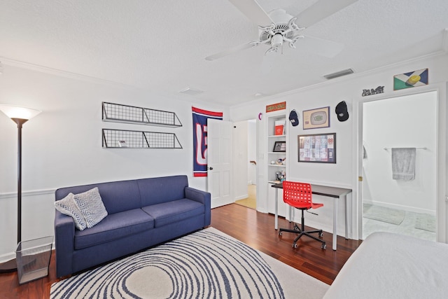 living room with a textured ceiling, ceiling fan, wood finished floors, visible vents, and ornamental molding