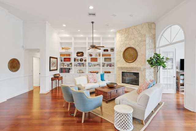 living room with a premium fireplace, wood finished floors, visible vents, built in features, and ornamental molding