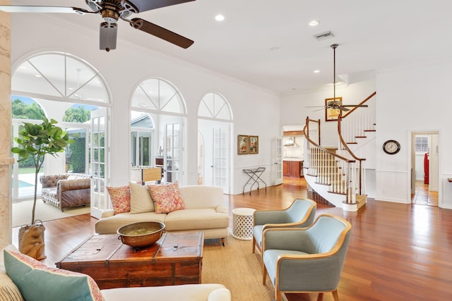 living room featuring crown molding, visible vents, ceiling fan, wood finished floors, and stairs