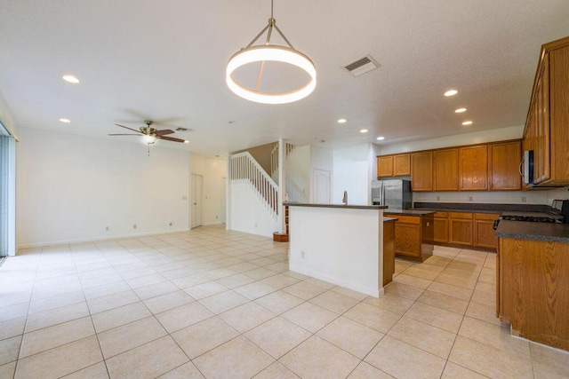 kitchen featuring brown cabinets, light tile patterned floors, stainless steel appliances, dark countertops, and visible vents