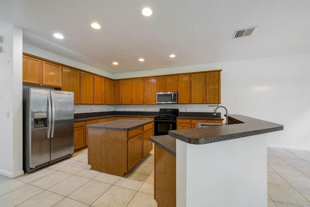 kitchen featuring light tile patterned floors, dark countertops, appliances with stainless steel finishes, a center island, and a sink