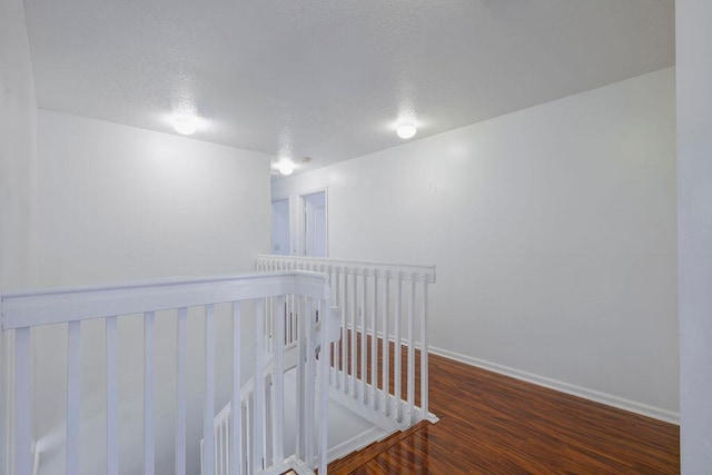 hall with a textured ceiling, wood finished floors, an upstairs landing, and baseboards