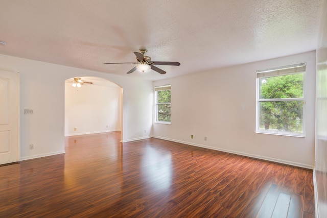 spare room with arched walkways, ceiling fan, a textured ceiling, baseboards, and dark wood-style floors