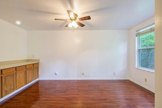 empty room featuring ceiling fan, a textured ceiling, baseboards, and dark wood-style flooring