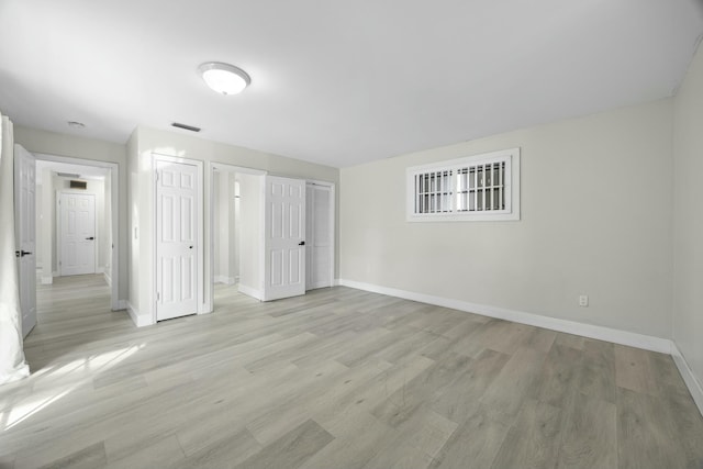 unfurnished bedroom with multiple closets, visible vents, light wood-style floors, and baseboards