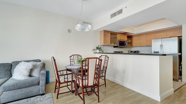 dining space with visible vents, light wood-style flooring, a raised ceiling, and baseboards