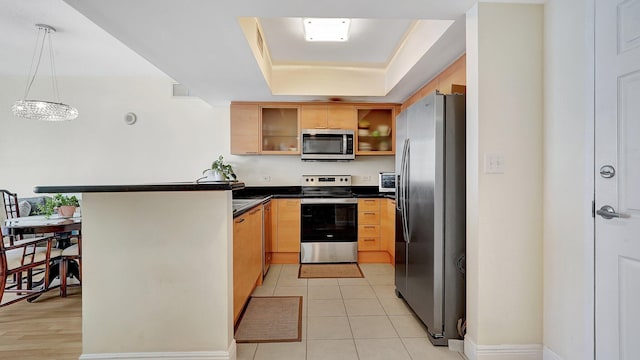 kitchen featuring a tray ceiling, dark countertops, appliances with stainless steel finishes, a peninsula, and light tile patterned flooring