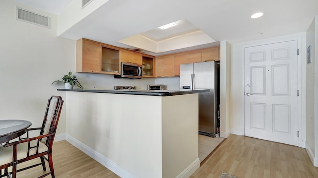 kitchen with visible vents, a peninsula, stainless steel appliances, light wood-style floors, and dark countertops