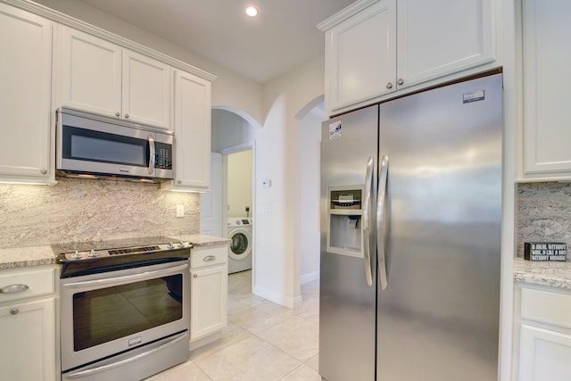 kitchen featuring washer / dryer, arched walkways, white cabinets, decorative backsplash, and appliances with stainless steel finishes