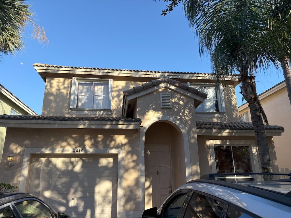 traditional-style house with a tiled roof, an attached garage, and stucco siding