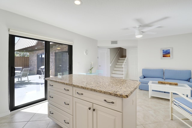 kitchen with visible vents, a kitchen island, light stone countertops, open floor plan, and light tile patterned floors