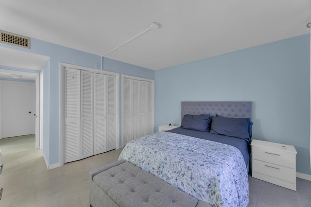 bedroom featuring baseboards, visible vents, multiple closets, and tile patterned floors