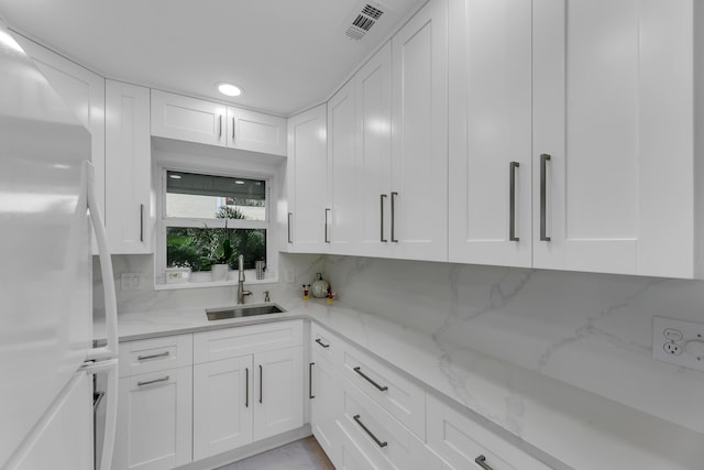 kitchen featuring freestanding refrigerator, a sink, light stone countertops, white cabinetry, and backsplash