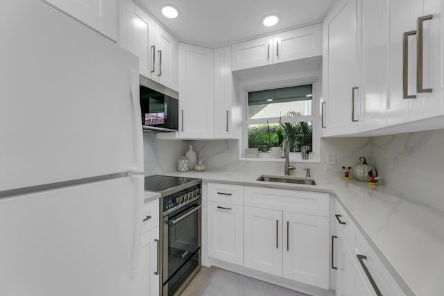 kitchen with backsplash, freestanding refrigerator, white cabinets, a sink, and high end range