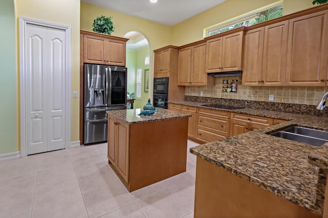 kitchen featuring light tile patterned floors, a sink, a center island, decorative backsplash, and black appliances