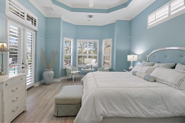 bedroom with visible vents, baseboards, light wood-type flooring, a tray ceiling, and crown molding