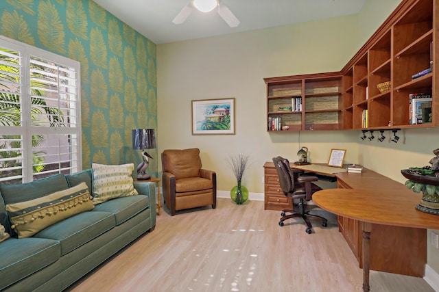 home office featuring wallpapered walls, baseboards, ceiling fan, light wood-type flooring, and built in desk