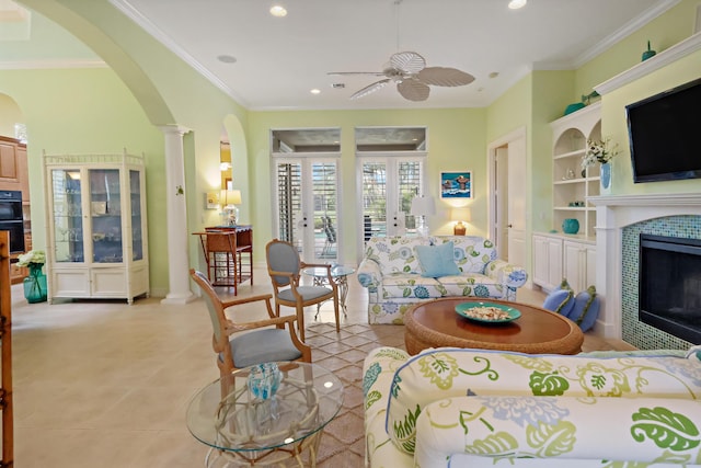 living room with built in shelves, arched walkways, crown molding, decorative columns, and a tile fireplace