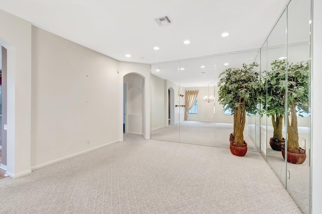 empty room with arched walkways, light carpet, recessed lighting, baseboards, and a chandelier