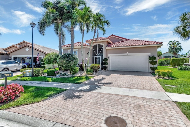 mediterranean / spanish house featuring stucco siding, an attached garage, a tile roof, decorative driveway, and a front lawn