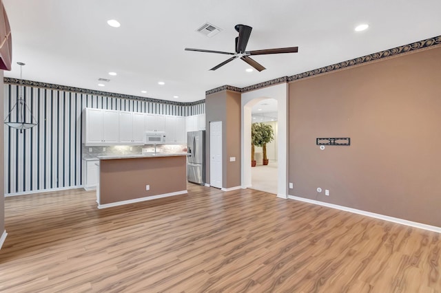 unfurnished living room with arched walkways, a ceiling fan, recessed lighting, light wood-style floors, and baseboards