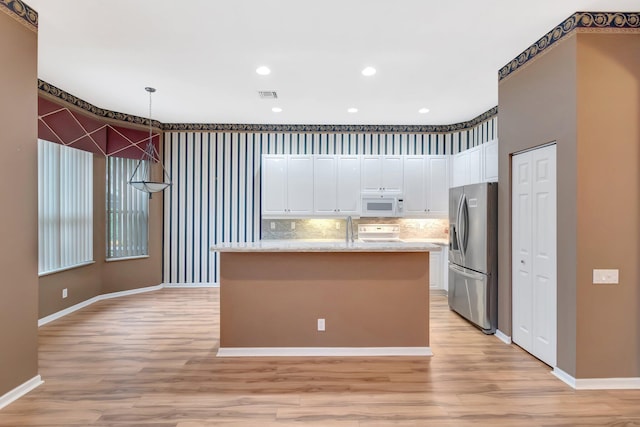 kitchen featuring white microwave, stainless steel fridge with ice dispenser, stove, light wood-type flooring, and white cabinets