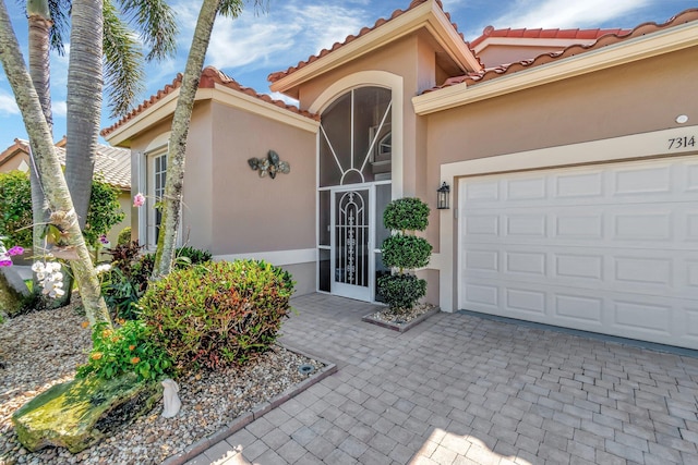 doorway to property with stucco siding, decorative driveway, a tiled roof, and a garage