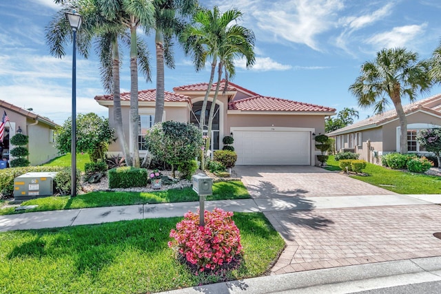 mediterranean / spanish-style house with an attached garage, a tile roof, decorative driveway, stucco siding, and a front lawn