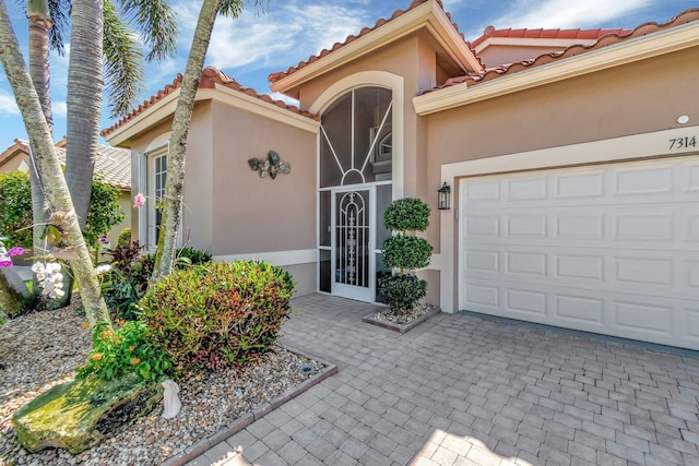 entrance to property with a tiled roof, decorative driveway, a garage, and stucco siding