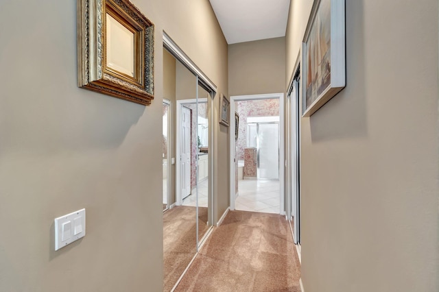 hallway with baseboards and light colored carpet