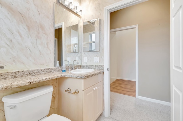 half bath with toilet, baseboards, and vanity