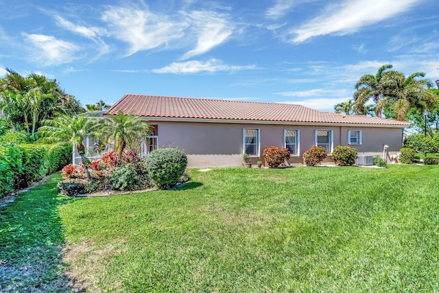 rear view of house featuring central air condition unit, stucco siding, a tile roof, and a lawn