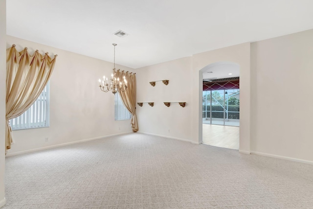 carpeted empty room featuring a chandelier, arched walkways, and baseboards