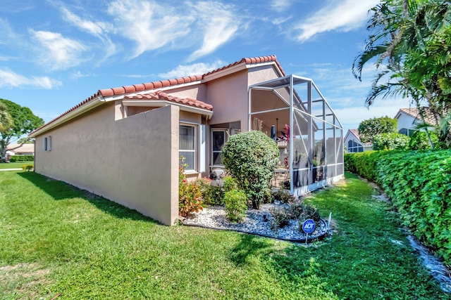 view of side of home with a tiled roof, stucco siding, a lawn, and a lanai