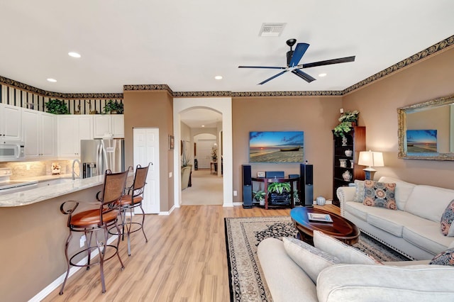 living area with a ceiling fan, arched walkways, light wood-style flooring, recessed lighting, and baseboards