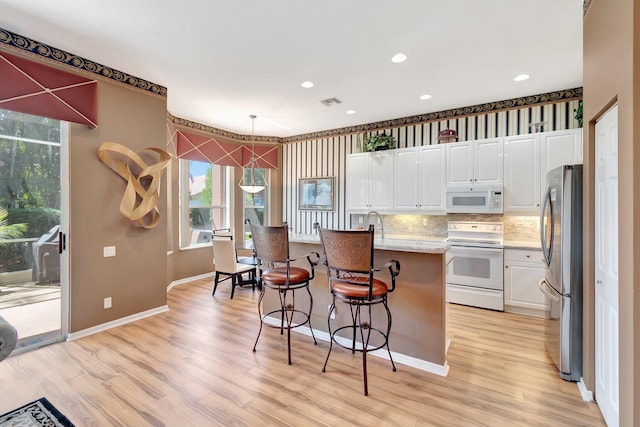 kitchen featuring white appliances, light wood finished floors, white cabinetry, a kitchen bar, and pendant lighting