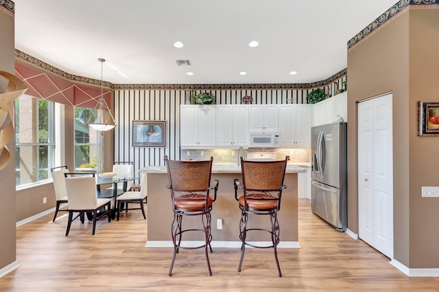 kitchen with stainless steel fridge, white microwave, light wood-style flooring, white cabinets, and recessed lighting